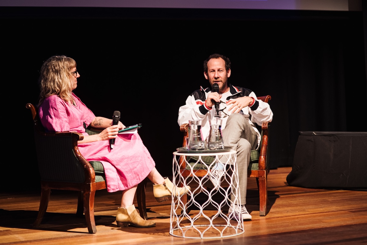 Two speakers seated on stage in armchairs having a panel discussion with microphones at the Regional and Remote Music Summit.